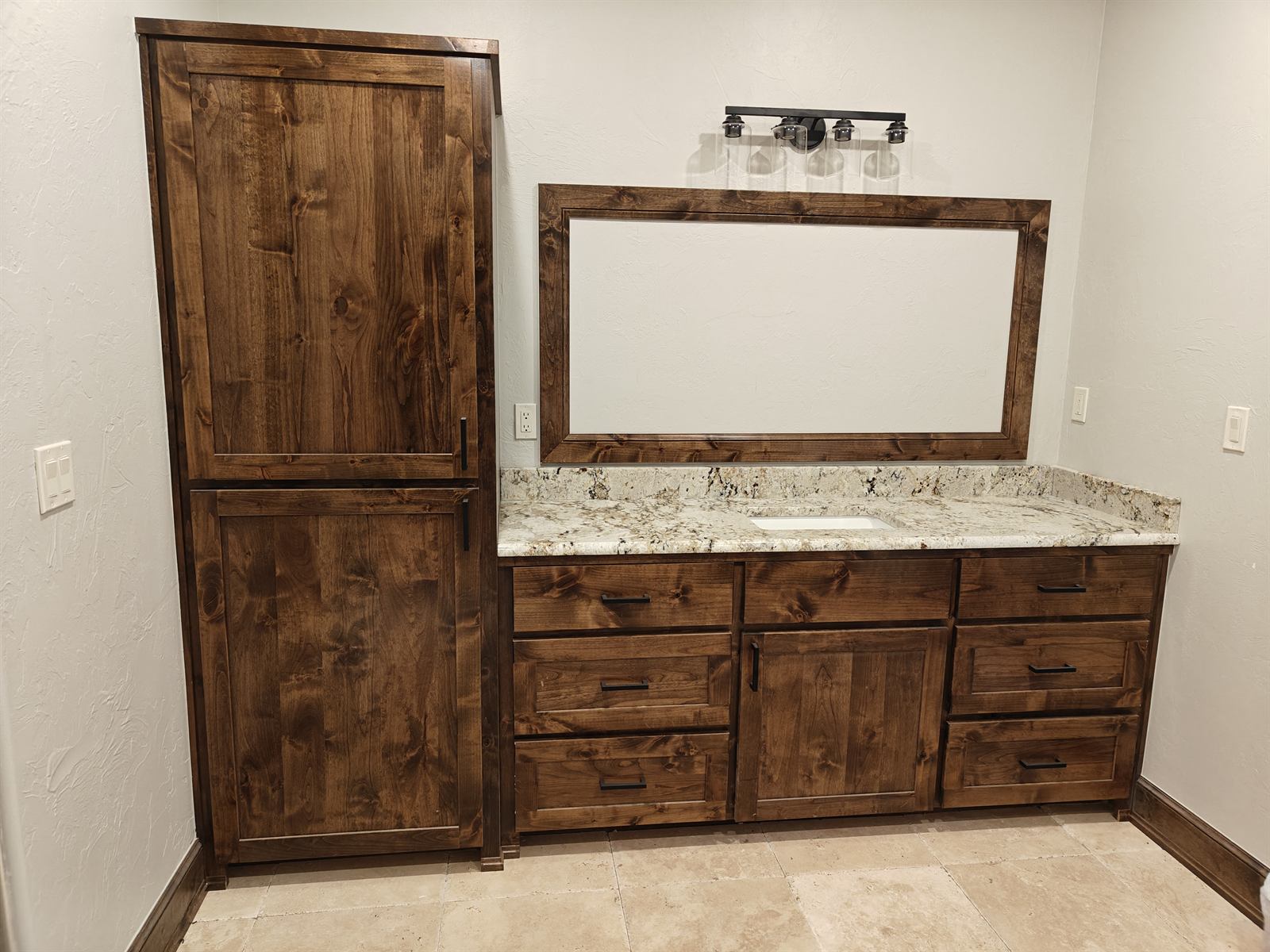 Custom dark-stained master bathroom vanity with matching linen tower and framed mirror