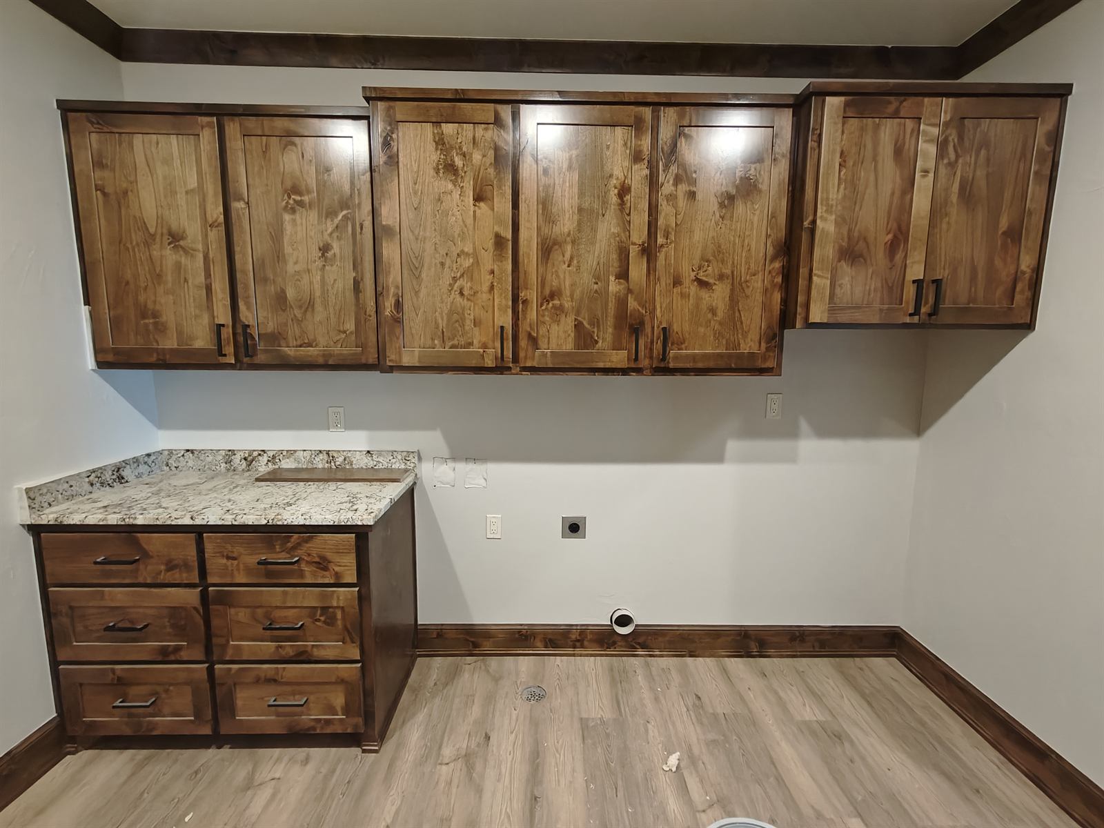 Custom dark-stained laundry room cabinets with granite countertop